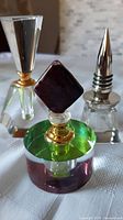 Three vintage crystal perfume bottles on a white fabric surface taken in natural to low lighting showing details of clear and colored glass and metal stopper.