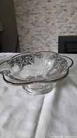 Front view of vintage crystal bowl with silver floral overlay on rim, placed on white patterned fabric with tiled wall background.