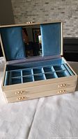 Open vintage jewellery box showing blue velvet compartments, mirror, and gold decorative handles.