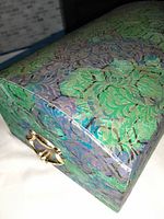Closed vintage jewellery box showing green and purple floral pattern and gold-tone pull handle on front.