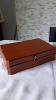Closed view of the rectangular vintage wooden jewellery box with curved edges and metal clasp, medium brown finish.