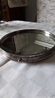 Full view of vintage round bar tray with reflective mirror base and tarnished silver plated rim on a white patterned cloth.