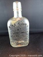 Front view of clear embossed glass A.M. Smith whiskey flask, showing raised lettering and overall condition