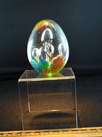 Front view of glass egg paperweight on acrylic stand showing multicolour interior petals