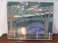 Framed fabric landscape artwork wrapped in plastic leaning on credenza top