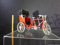 Full side view of red tricycle rickshaw model on display stand