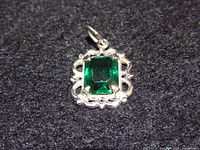 Front view of silver-tone pendant showing emerald-cut green stone and ornate frame