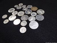 All twenty-three silver-tone world coins laid out on dark surface