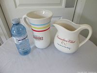 Overview showing both branded ceramic pitchers with water bottle for scale
