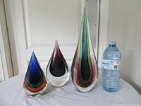 Front view of three glass teardrop sculptures beside water bottle for scale