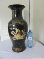 Front view of black vase showing lotus flower and bird artwork next to water bottle for scale