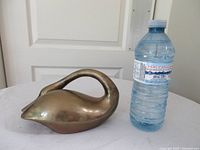 side view of solid brass swan next to water bottle for scale