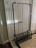 Full view of black metal garment rack with shoe shelves and casters