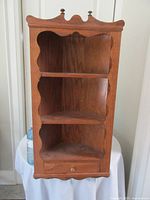 Front view showing scalloped edges, shelves, drawer, decorative top