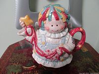 Front view of multicoloured patchwork angel teapot showing facial details, red handle and spout