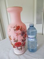 Front view of pink floral glass vase beside water bottle for scale