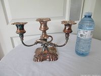 Front view of three-arm silverplate candelabra beside water bottle for scale