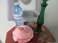 Overall shot showing pink jewelry case, clear Avon perfume bottle, tall green glass decorative bottle on a surface