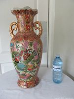 Front view of tall ornate vase beside water bottle for scale