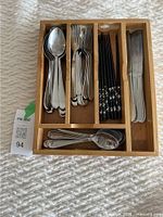 Top-down view of wooden drawer divider containing large spoons, large forks, chopsticks, knives, and smaller spoons.