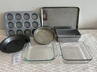 Photo showing all baking pans and dishes arranged, including muffin pan, cookie sheet, round cake pans, loaf pans, pie dish, and glass baking dishes.