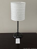Front view of bedside table lamp with white paper lampshade on black glossy base.