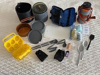 Full overview of the camping kitchen set with pots, bowls, lids, utensils, storage bags, and accessories laid out on fabric surface
