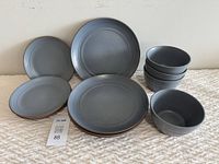 Set of 4 dinner plates, 4 side plates and 4 bowls in matte blue-grey ceramic with concentric ring texture, displayed on beige textured surface