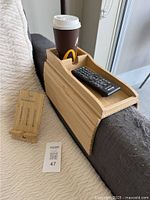 Tray table fitted around an armrest holding a paper coffee cup and a remote, with cell phone stand beside it.