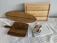 Photo showing the five items: large bamboo cutting board, oval wooden charcuterie board, smaller wooden cutting board, white plastic cutting board, and bamboo serving utensil set.