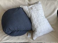 Pile shows dark blue duvet and white pillow on beige fabric surface.