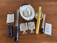 Photo showing six kitchen tools: two handheld graters with black handles, two small stainless steel cheese graters, white plastic citrus juicer, yellow citrus squeezer, and metal cocktail muddler.