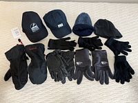 Photo showing a collection of hats and gloves laid out on a white surface, including two baseball caps, a knitted toque, fleece beanie, Marmot mitts, fleece gloves, leather work gloves, and liner gloves.