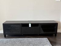 Black IKEA Besta TV storage bench with two glass doors on sides, central open shelf, and drawer below