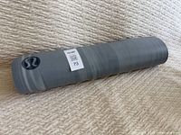 Rolled grey yoga exercise mat showing the Lululemon logo on the side with manufacturer and lot barcode sticker.