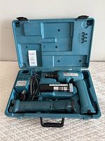 Makita drill, charger, flashlight baton in blue case on white surface