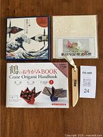 Origami handbook, unopened patterned paper, open pack of Mt Fuji patterned paper, and wooden folding tool on wooden table.