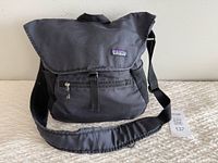 Closed front view of the black Patagonia messenger bag with adjustable strap and front zip pocket.