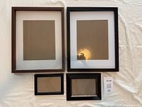 Front view of four photo frames displaying white and brown mattes; two large wood frames and two smaller plastic frames.