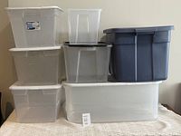 Photo of six plastic storage boxes stacked, showing variety of brands and sizes including extra-long white box, three Sterilite boxes, dark grey Rubbermaid box, clear box with black lid, and smaller IKEA box.