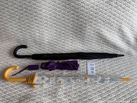 Three umbrellas laid flat showing black Fulton umbrella, purple collapsible umbrella, and clear umbrella with daisy print fully closed
