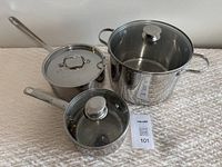 Photo of three stainless steel pots on a textured fabric surface along with two glass lids and one stainless steel lid.