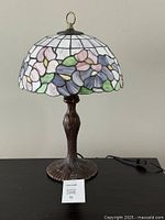 Full view of Tiffany style stained glass table lamp with floral shade and ornate metal base showing cord and pull chain.