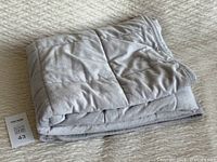 Folded light grey weighted blanket displayed with a MaxSold lot tag number 43.