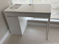 Photo showing front view of the white IKEA Micke desk with closed drawers and cabinet door, cord management hole on top.