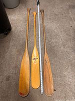 Front view of all three wooden canoe paddles alongside measuring tape