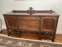 Front view of carved Jacobean/Baroque Revival wooden sideboard buffet showing doors, drawers, backsplash, turned legs, stretcher base