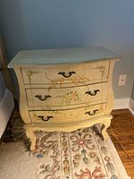 Front view of hand-painted bombe nightstand showing three drawers, hardware, floral motif