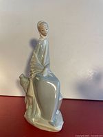 Full view of porcelain figurine showing seated maiden, bird at side, overall glaze and condition