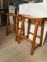 Two medium brown wooden Tibetan style counter stools positioned beside kitchen island showing general condition and full stool structure.